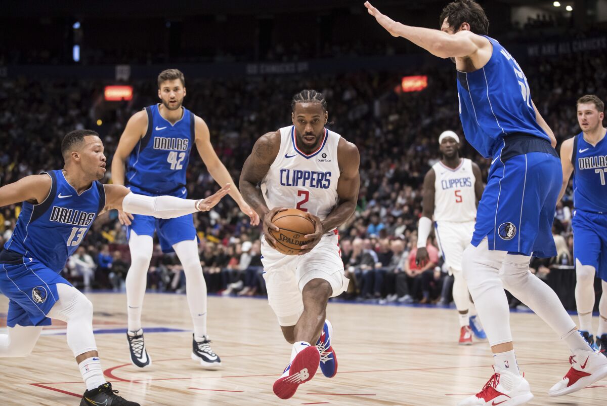 Clippers star Kawhi Leonard drives past Jalen Brunson, left, and Luka Doncic, right, of the Dallas Mavericks during the Clippers' preseason loss Thursday.