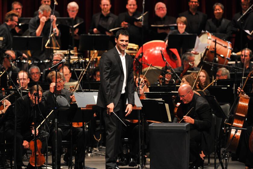 A conductor in a suit standing in front of an orchestra