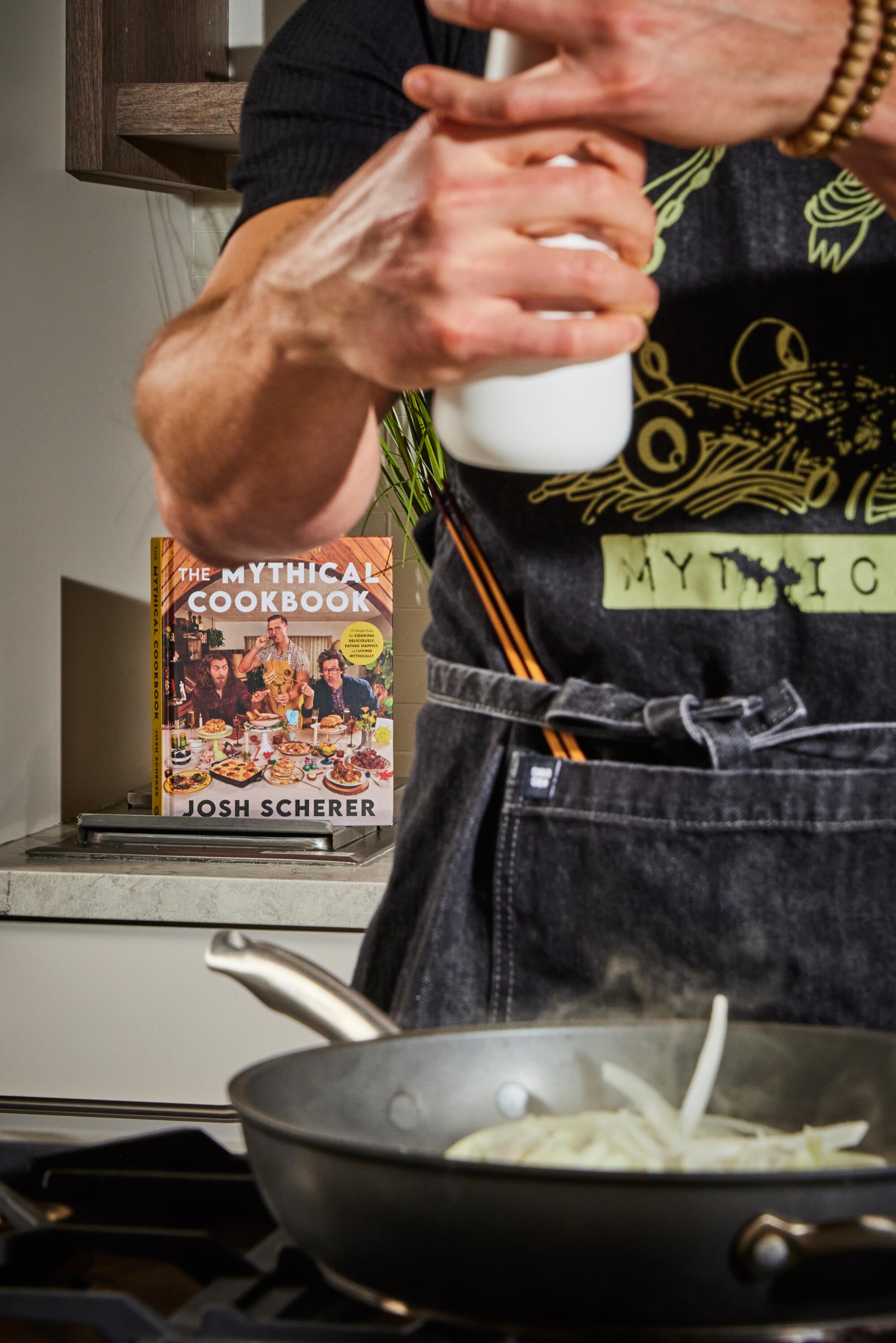 Josh Scherer cooks onions in the L.A. Times Test Kitchen. Behind him is a copy of his cookbook.