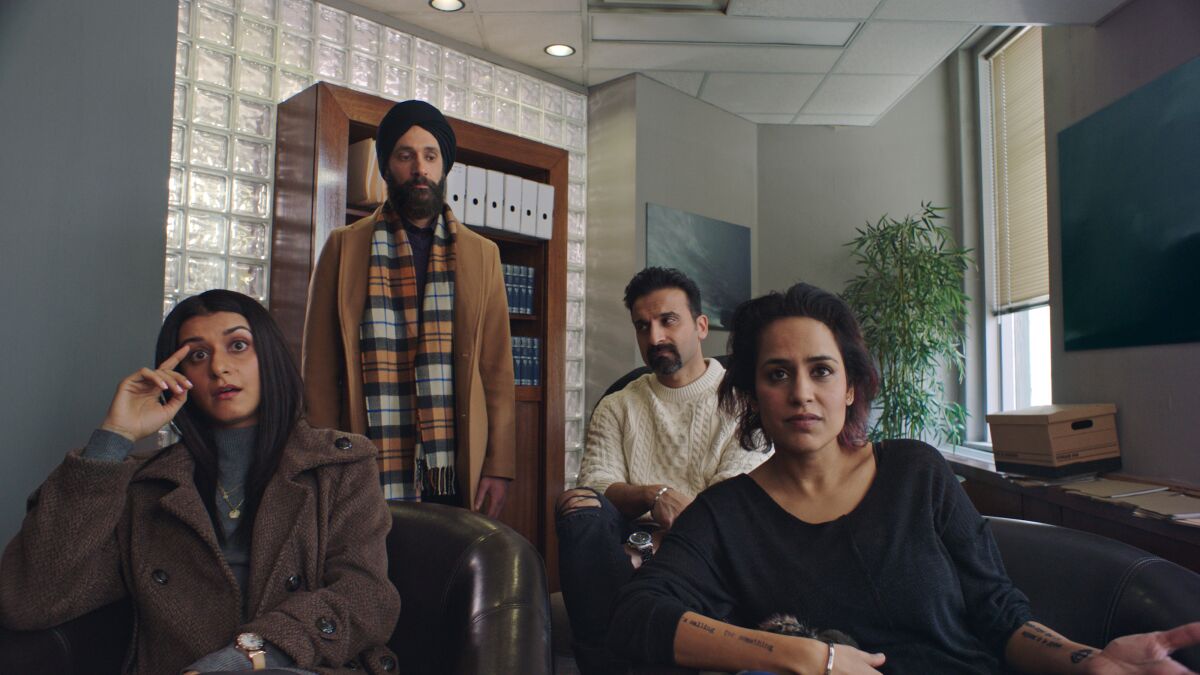 Two women and a man sitting and one man standing inside an office.