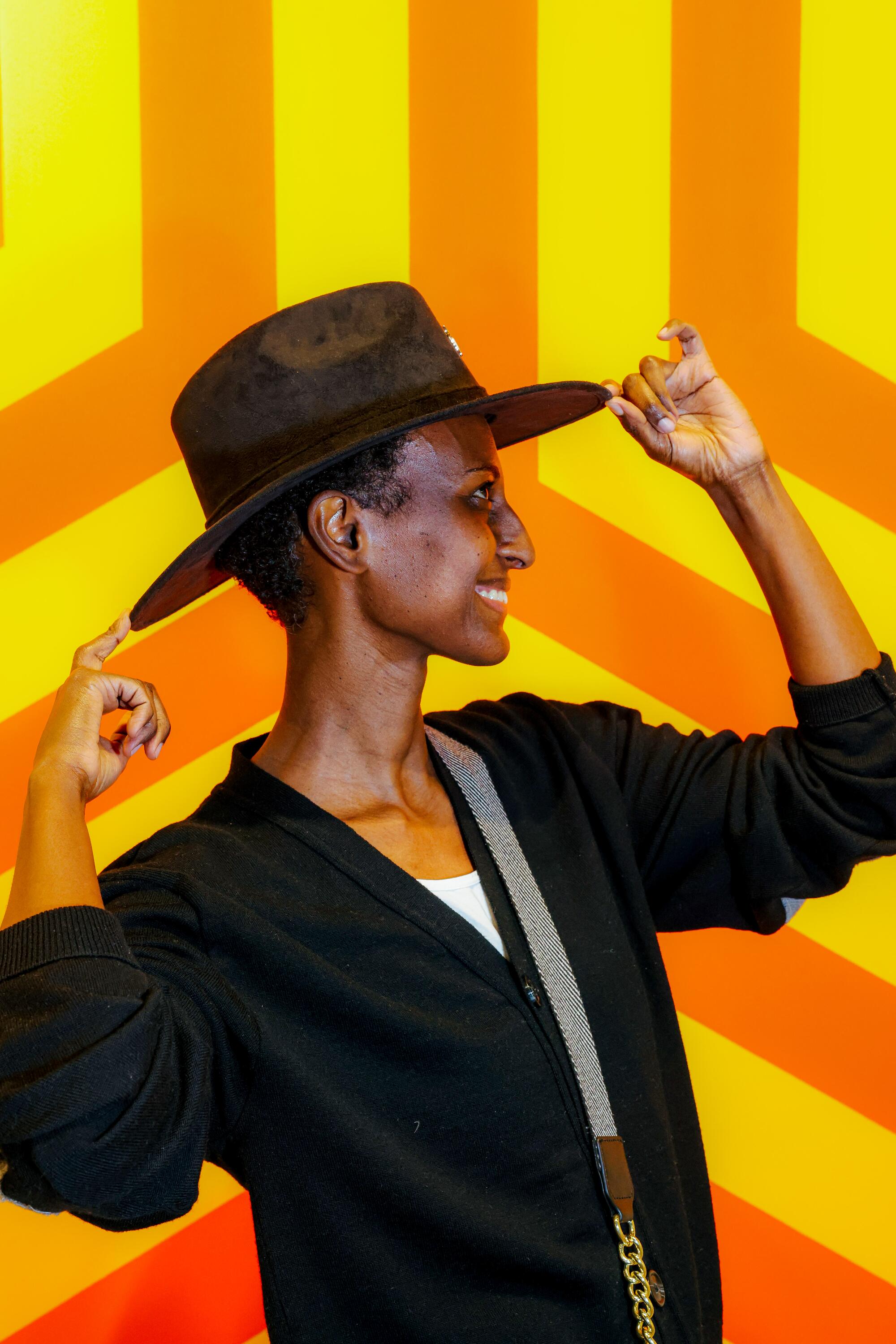 A person poses in front a work of art, tipping their hat.