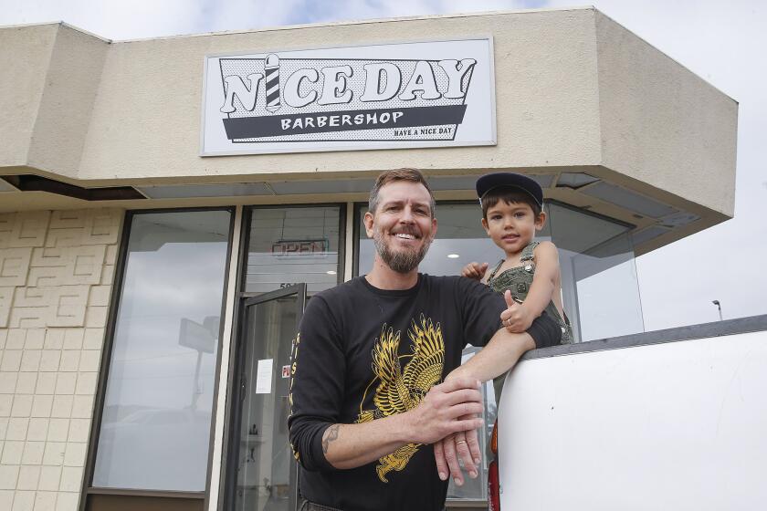 Jake Bushnell with his son Rocky, under his new sign for Nice Day Barbershop, a beach-vibe barbershop in the Westfair Shopping Center in Huntington Beach.