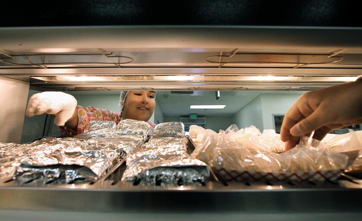 Kitchen worker Andrea Jimenez, left, keeps the food stocked as a student grabs food items in the cafeteria lunch line at Bravo Medical Magnet High School in Los Angeles.