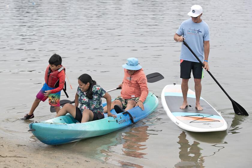 Alexander Hernandez, far left, steps off a kayak after paddling across the bay with his parents Adelyn and Giovanni, as camp volunteer Tom Swanecamp guides them as they participate in the Miracles for Kids, 13th annual "Surf & Paddle" summer camp for families of critically-ill children at the Newport Dunes Waterfront Resort and Marina in Newport Beach on Thursday.