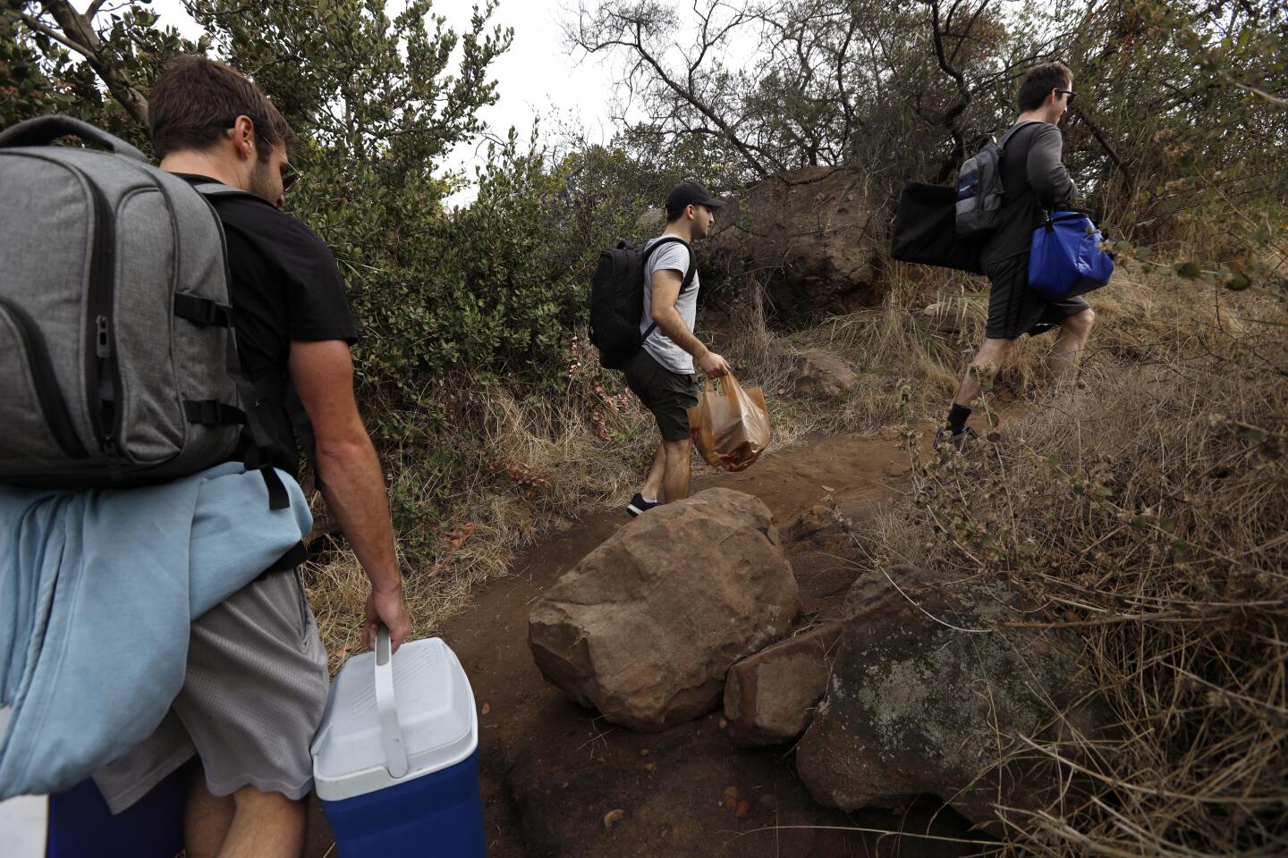 PACIFIC PALISADES, CA - NOVEMBER 30, 2019 - Jack Petros, 28, from left, Dylan Skolnik, 24, and David Weber, 27, members of the Summit Sippers, hike along the Liones Trail in Pacific Palisades on November 30, 2019. Summit Sippers set up impromptu little bars at random view spots on L.A. hiking trails. They wear bow ties, suspenders and one wears a top hat. They are all avid hikers who enjoy the experience of hiking and than setting up their impromptu watering hole. The drinks are free and they won't even take tips. They are careful not to leave trash behind or block spots where hikers might like to take photos. They try and find picturesque sites along LA’s hiking trails. (Genaro Molina / Los Angeles Times)