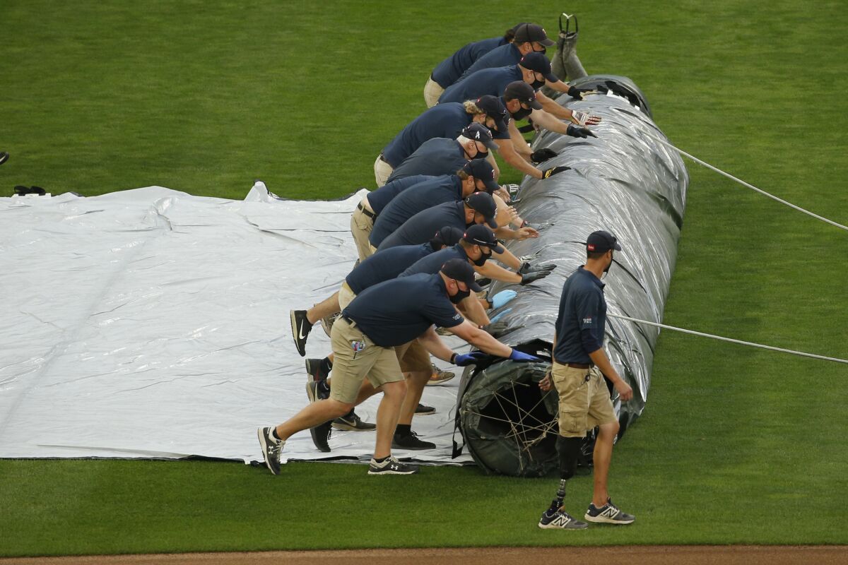 Minnesota Twins grounds crew members roll out a tarp for expected rain which has delayed the start of a baseball game with the Kansas City Royals on Friday, Aug. 14, 2020, in Minneapolis. (AP Photo/Bruce Kluckhohn)
