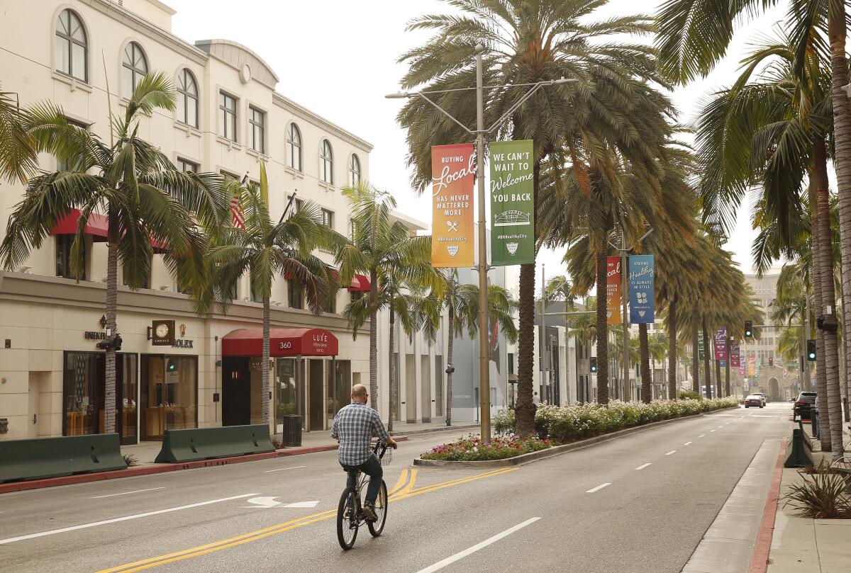 A man rides a bicycle on palm tree-lined Rodeo Drive in Beverly Hills.
