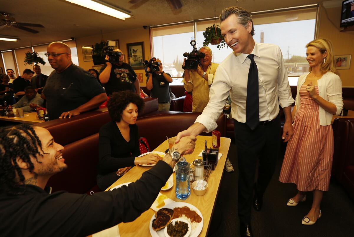 Gavin Newsom with his wife Jennifer Siebel Newsom, right, greet Andre Truth, left, and Zhani Jackson at The Serving Spoon in Inglewood.