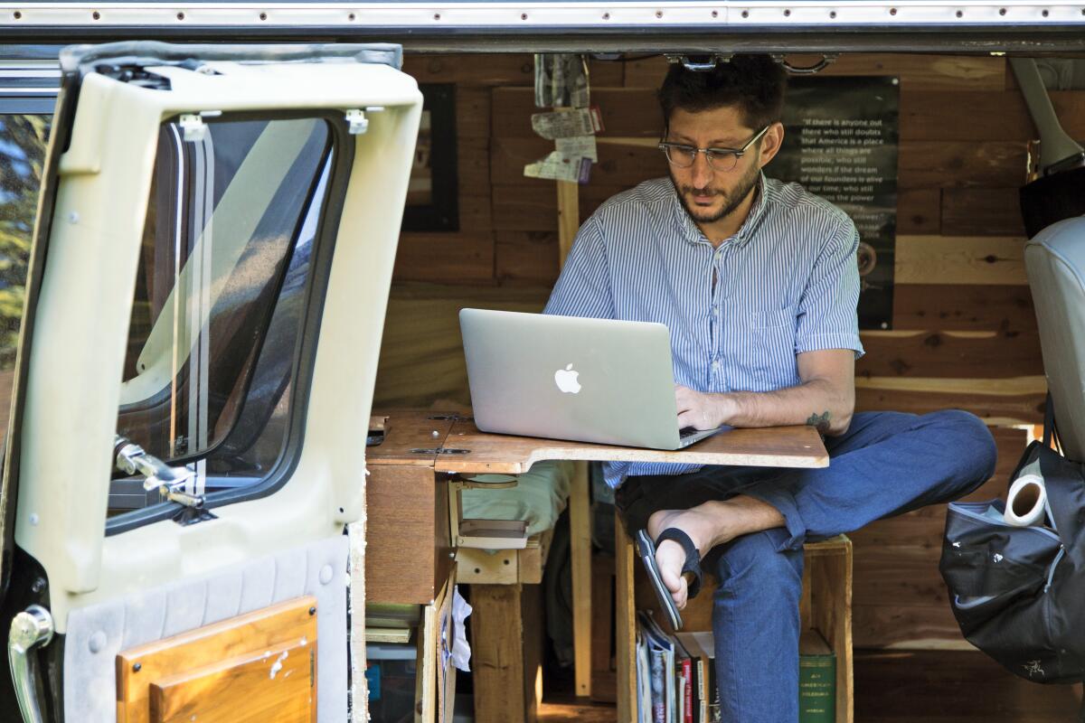  A bearded man with glasses works on his laptop inside a van 