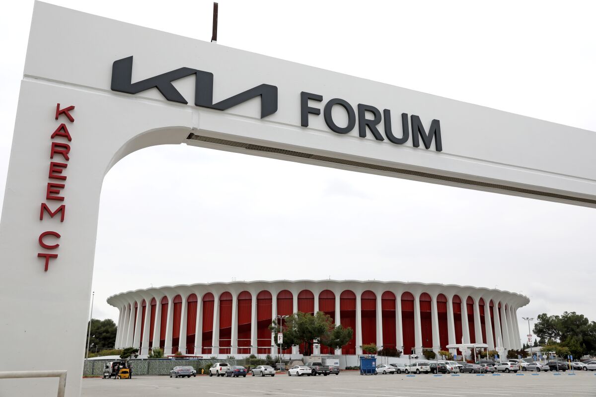 An arch with the words "Kia Forum" stands in front of a parking lot and an arena.