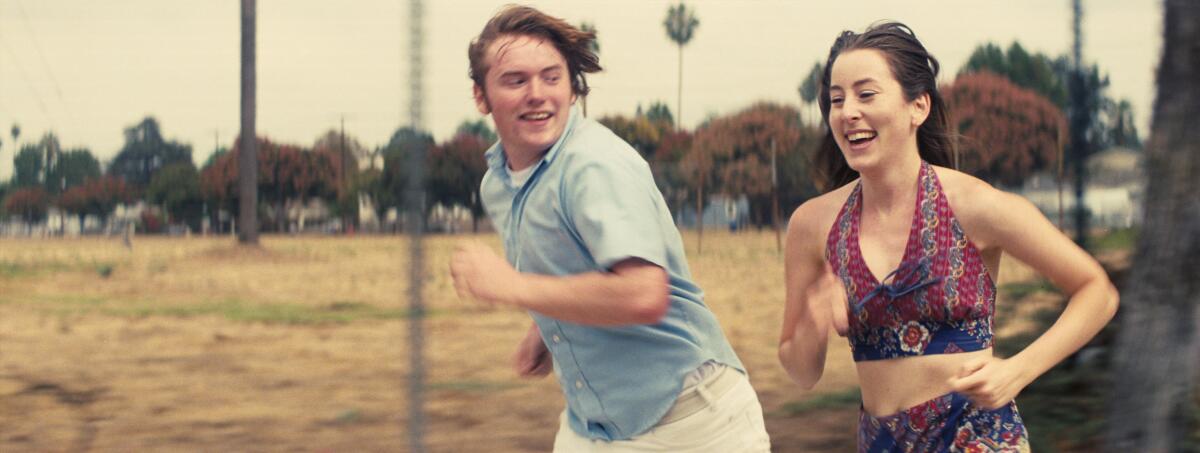 A young man and woman laugh as they run by an open field.