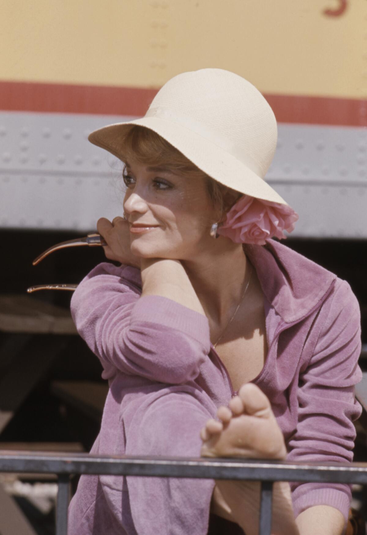 Lynne Marta, in a hat, has a relaxed smile as she rests her head on her arm, her outstretched foot rests on a metal rail