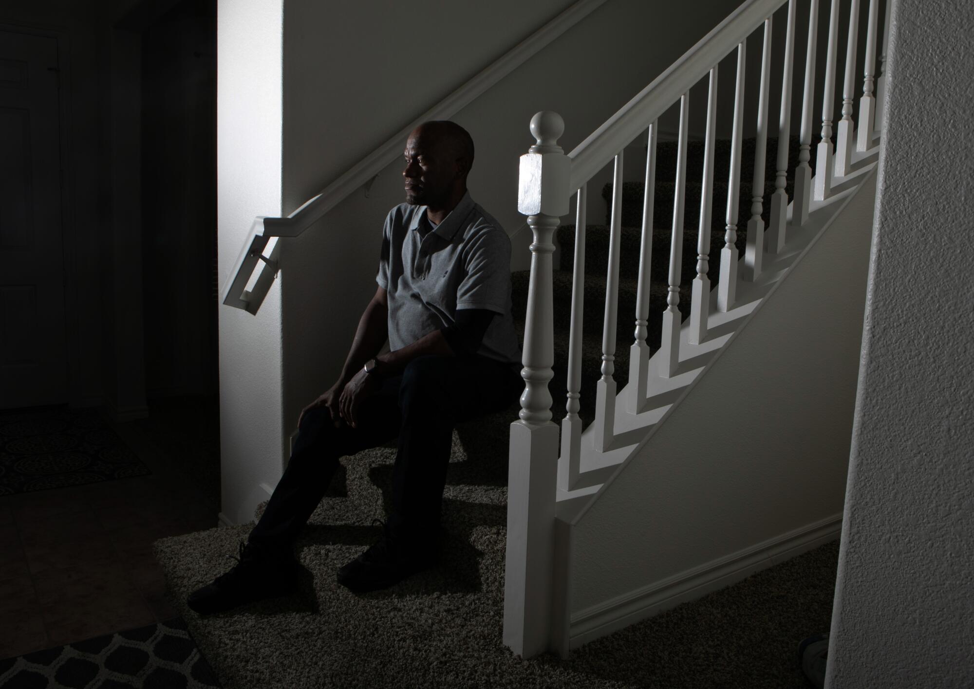 Man sits on stairs inside house.