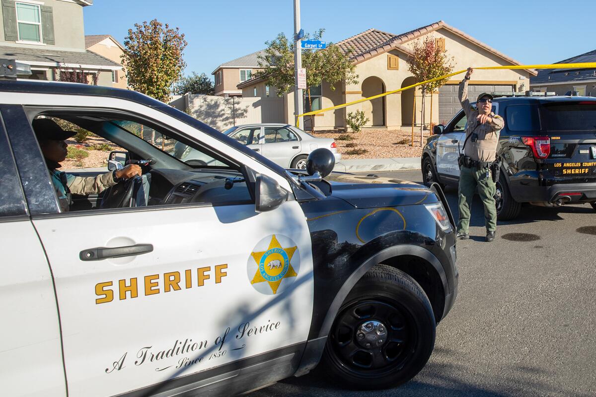 A law enforcement officers raises yellow tape to allow a sheriff's car to drive underneath it.