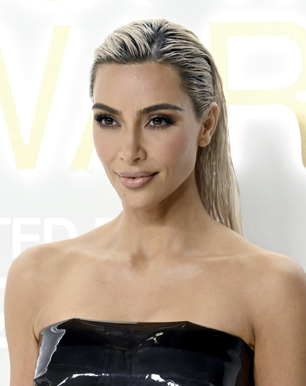 Kim Kardashian poses with slicked-back bleached hair in a black latex dress
