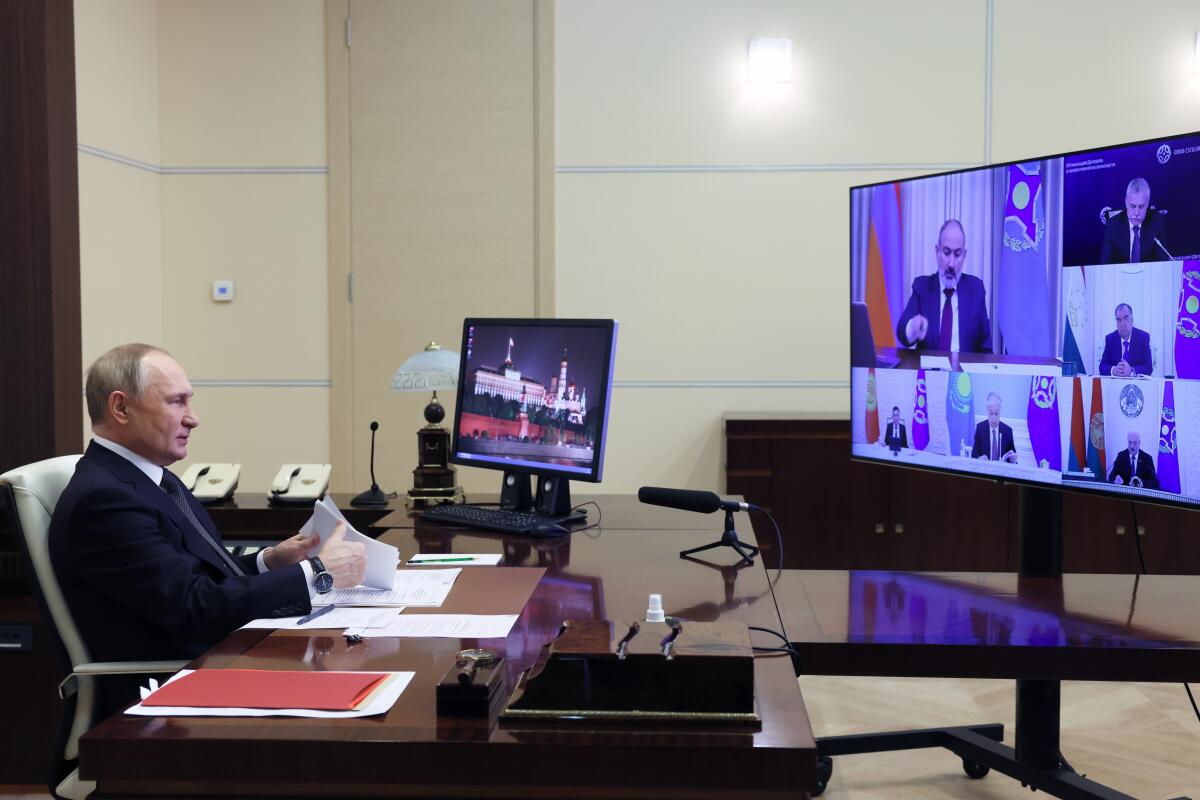 Russian President Vladimir Putin sits at a desk in front of electronic screens.