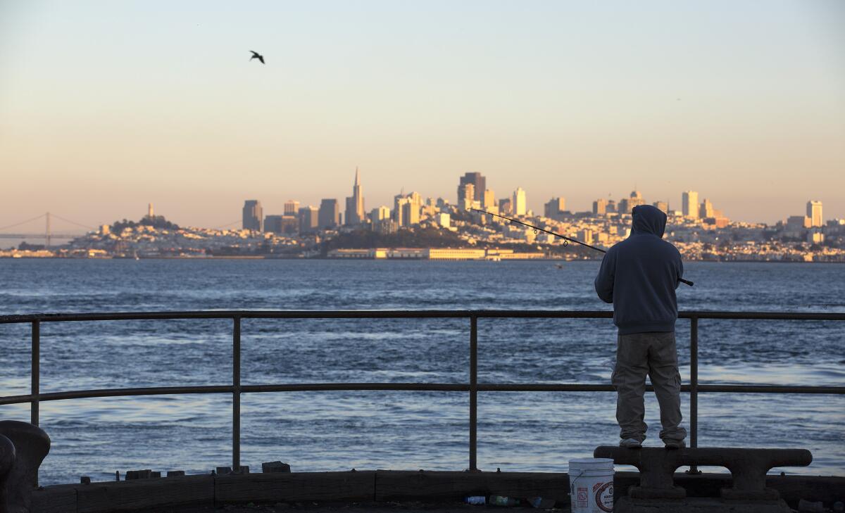 A fisherman has the San Francisco skyline to look at as he tries the water off a pier in Horseshoe Bay.