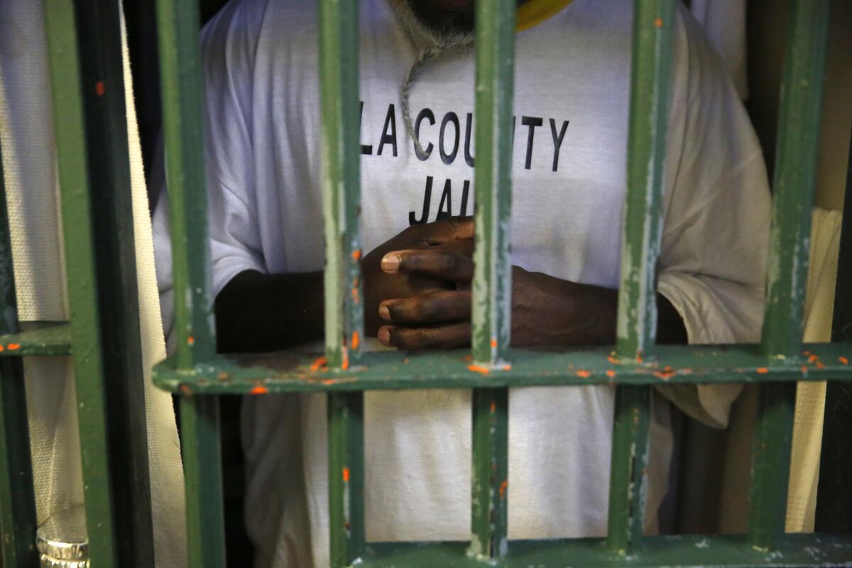 An inmate seen through bars wears a shirt reading "L.A. County Jail."