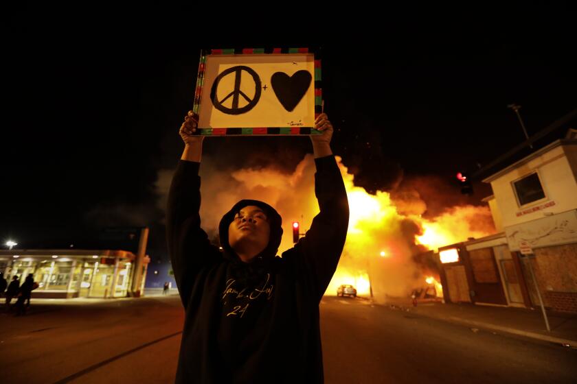 MINNEAPOLIS, Minnesota -MAY 29, 2020-One woman expresses her desire for peace and love. Despite a curfew, protests and looting went all throughout the night in various parts of the city of Minneapolis on Friday night, May 29, 2020. . There were too many fires for firemen to put out on Friday night, May 29, 2020. Protesting continues for a third day in response to the death of George Floyd. (Carolyn Cole/Los Angeles Times
