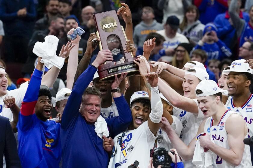 Kansas head coach Bill Self and players hold up the winning trophy after a college basketball game.