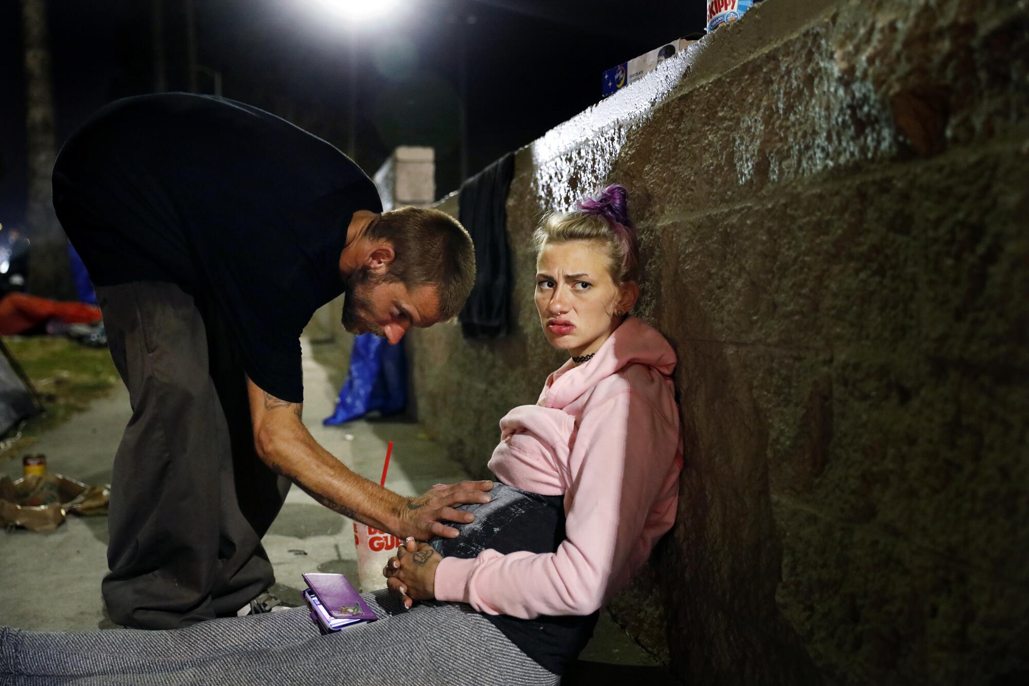 Mckenzie Trahan, 22, stares off as her boyfriend Eddie, 26, rests his hand on her stomach near their tent in Hollywood.