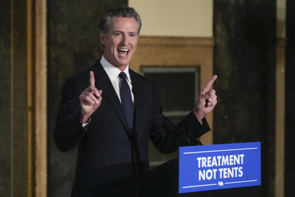 California Gov. Gavin Newsom points up while standing at a lectern.