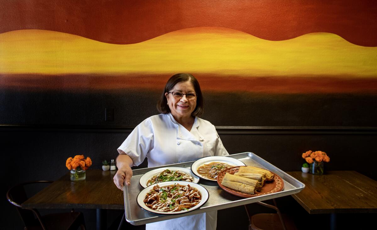 A smiling woman holds a tray with Mexican dishes.