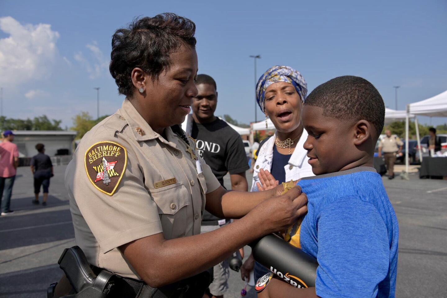 Baltimore deputy sheriff Carol Canty pins a toy badge on Zayvion Davis, 8 of Reservoir Hill with grandmother Lauren Muhammad and cousin Khalil Davis, 15 looking on at a National Night Out event at Mondawmin Mall on August 6, 2019.
