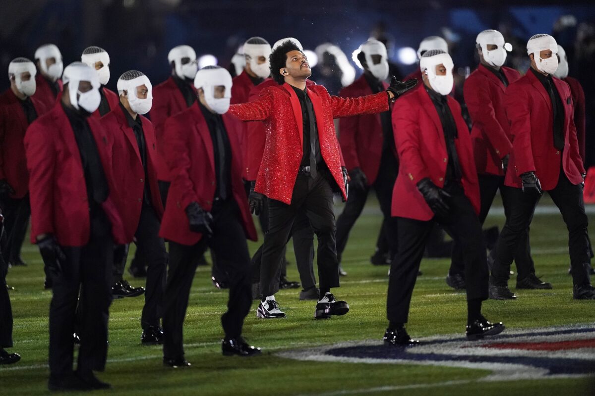The Weeknd and men in red jackets, white facial bandages and masks and black pants, at halftime of Super Bowl LV in 2021. 