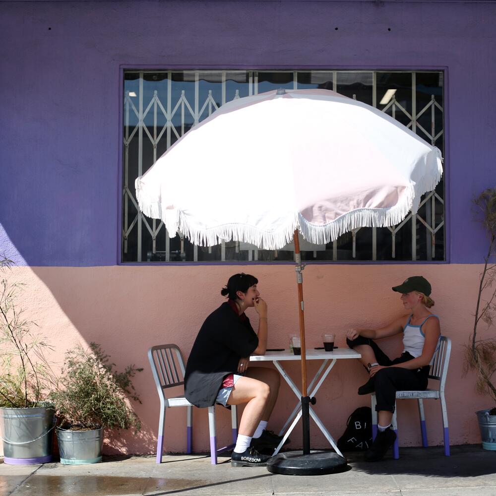 Two women sit at a cafe table under a white umbrella