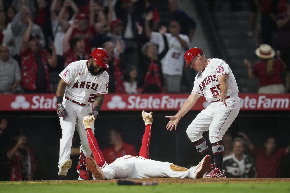 Los Angeles Angels designated hitter Shohei Ohtani, center, celebrates with Luis Rengifo (2) and third base coach Brian Butterfield (55) after sliding in to home to score during the ninth inning of a baseball game against the Baltimore Orioles Friday, July 2, 2021, in Anaheim, Calif. The run won the game for the Angels 8-7. (AP Photo/Ashley Landis)