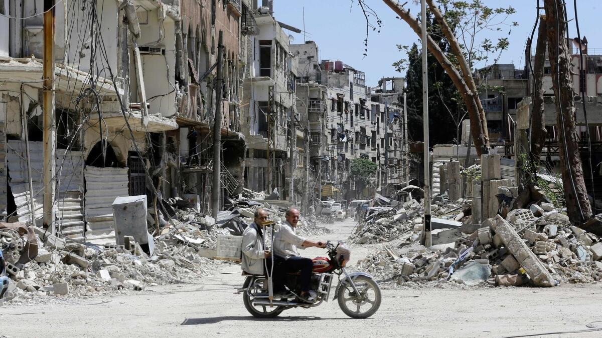 Syrians ride a motorcycle along a destroyed street in Duma on the outskirts of Damascus on Monday,