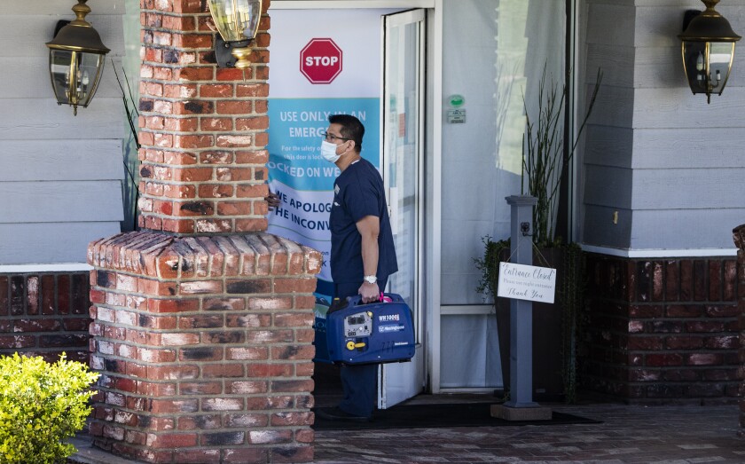 A medical staff member carries a digital inverter generator into Cedar Mountain Post Acute nursing home after 51 residents and six staff members tested positive for the coronavirus on Wednesday in Yucaipa. Two of the residents have died.
