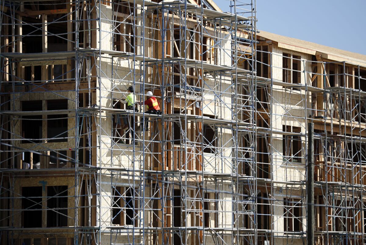 An apartment building is seen under construction, covered in scaffolding with two workers standing on it.