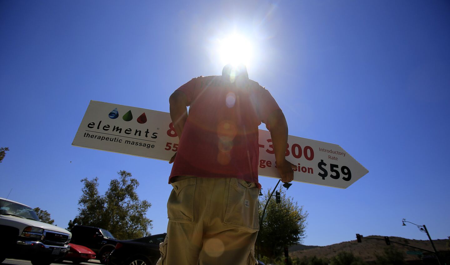Sign spinner Orlando Reyes points cars to a Thousand Oaks Blvd. massage business under the hot sun.