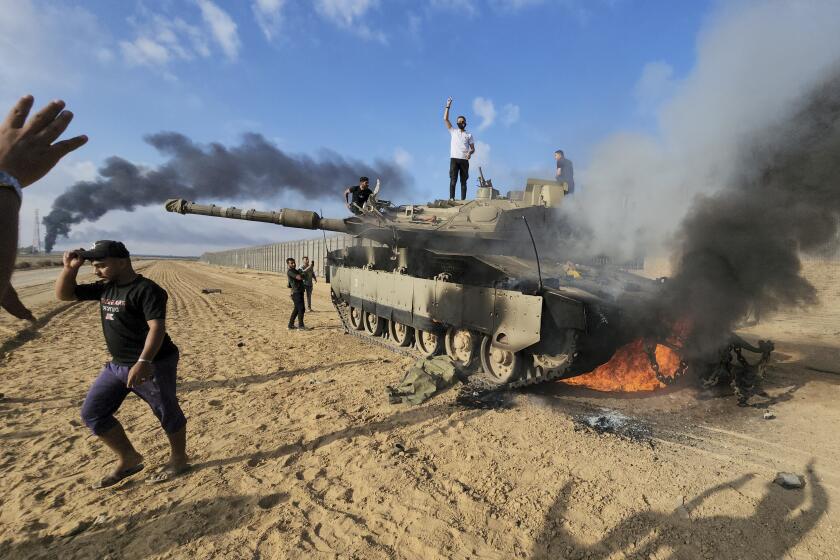 Palestinians celebrate by a destroyed Israeli tank at the Gaza Strip fence east of Khan Younis southern Saturday, Oct. 7, 2023. The militant Hamas rulers of the Gaza Strip carried out an unprecedented, multi-front attack on Israel at daybreak Saturday, firing thousands of rockets as dozens of Hamas fighters infiltrated the heavily fortified border in several locations by air, land, and sea and catching the country off-guard on a major holiday. (AP Photo/Hassan Eslaiah)