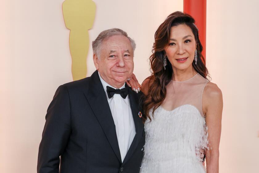 Jean Todt in a tuxedo puts his arm around actor Michelle Yeoh in a white gown at the Oscars