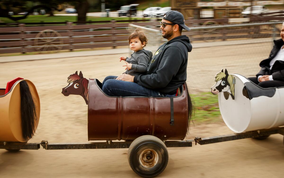 A man and a toddler ride in a barrel train made to look like a train of ponies.