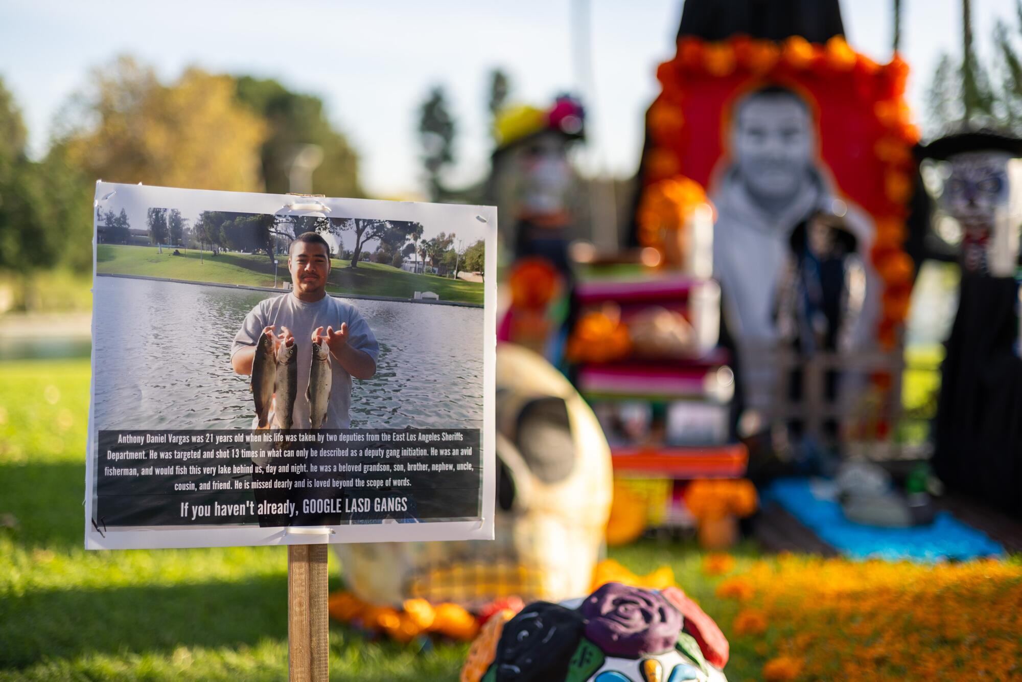 A photo of a man holding up two fish by a lake, in front of a Dia de los Muertos altar honoring him.