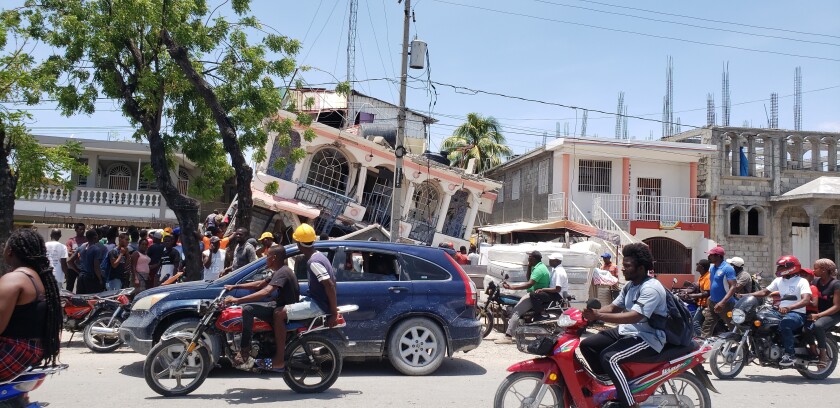 Damaged Petit Pas Hotel leans to one side while traffic passes in front of it