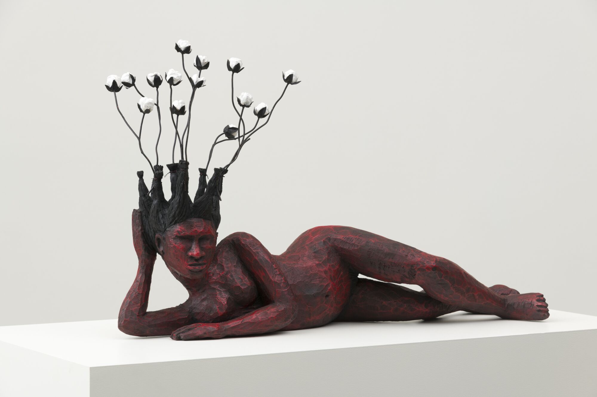 A reclining Black woman carved from wood sprouts cotton from her head