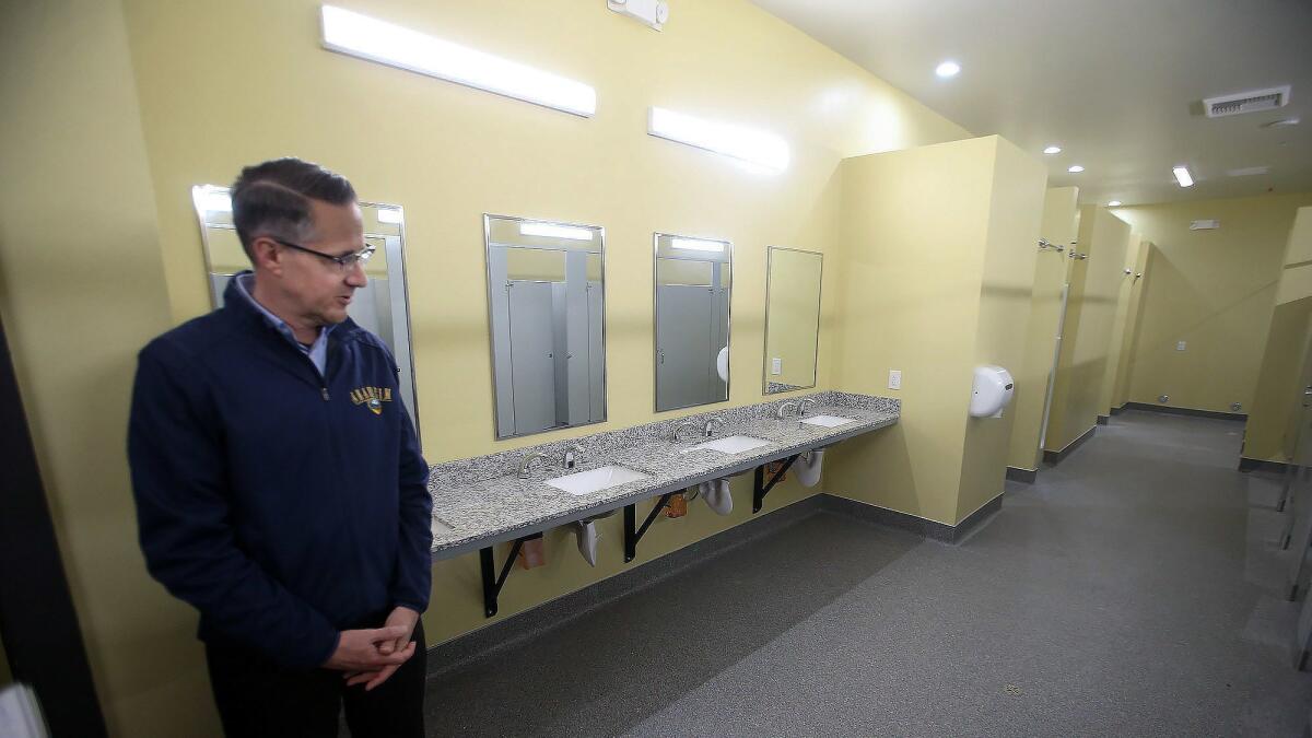 Mike Lyster, the city of Anaheim’s chief communications officer, stands in one of the bathrooms in the new homeless shelter on La Mesa Street.