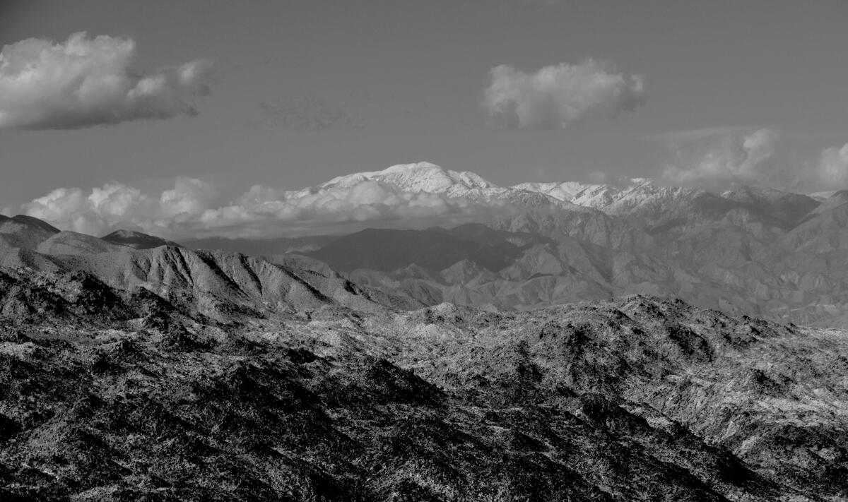 A black and white image of a snow-capped peak within a mountain range.