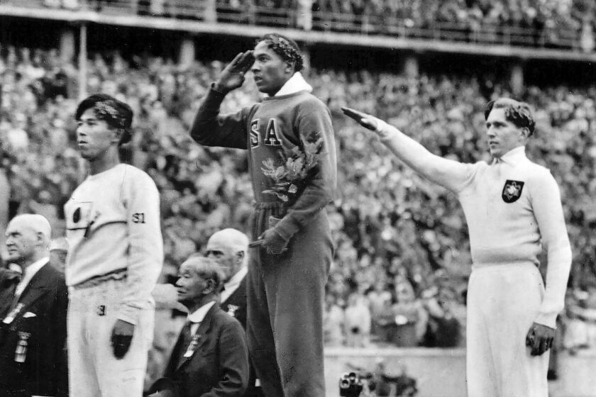 FILE - In this Aug. 11, 1936, file photo, America's Jesse Owens, center, salutes during the presentation of his gold medal for the long jump on, alongside silver medalist Luz Long, right, of Germany, and bronze medalist Naoto Tajima, of Japan, during the 1936 Summer Olympics in Berlin. Long's family has decided to auction his silver medal and other collectibles from his career, which was cut short when he was killed in World War II in 1943. (AP Photo/File)