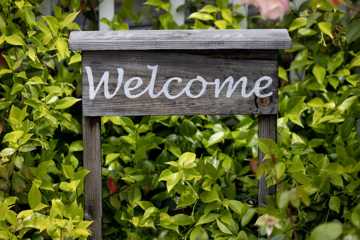A wooden welcome sign nestles in a bush in a front yard.