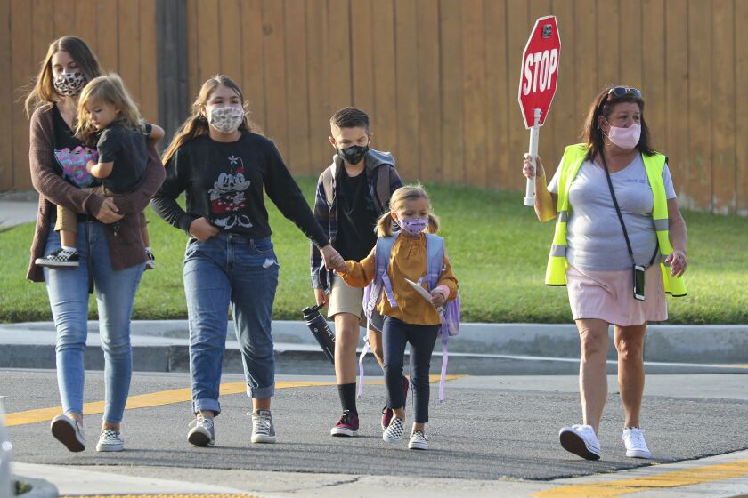FOUNTAIN VALLEY, CA - SEPTEMBER 23: A crossing guard help cross the street as students return, after months of closure due COVID-19 pandemic, at James H Cox Elementary School on Wednesday, Sept. 23, 2020 in Fountain Valley, CA. (Irfan Khan / Los Angeles Times)