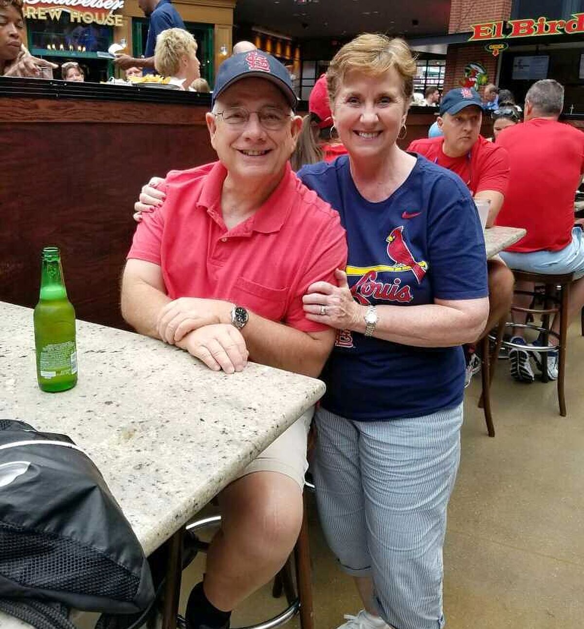 A couple in St. Louis Cardinals gear pose for a photo in a food court.