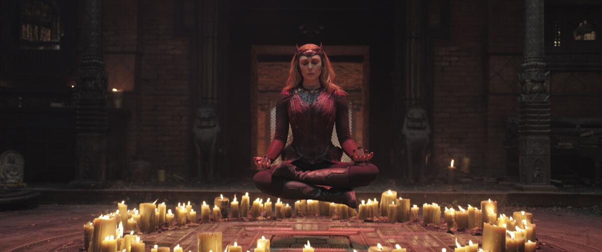A woman in a red bodysuit and crown sitting in front of a circle of candles