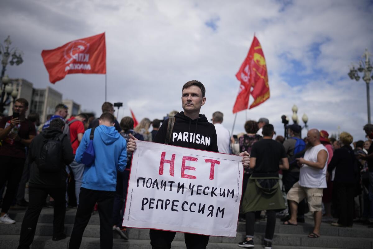 A man stands amid a crowd holding a sign with Russian words.