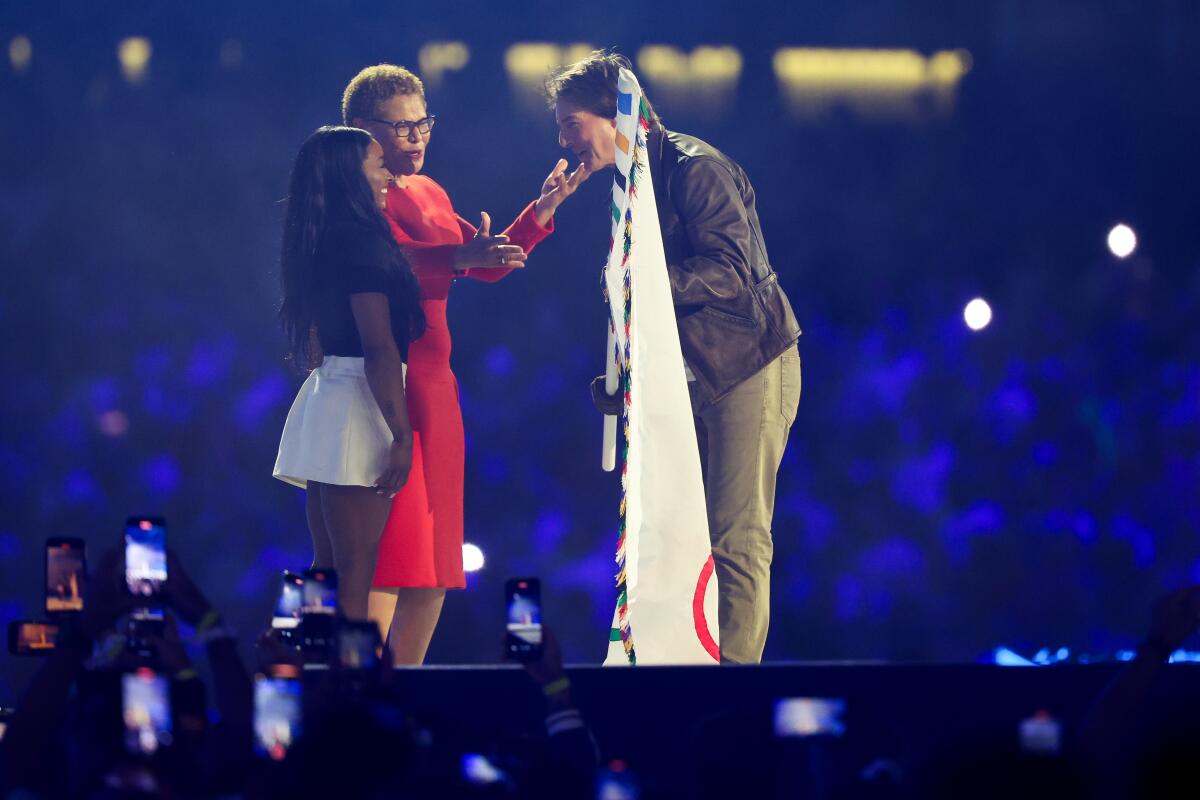 Tom Cruise holds the Olympic flag as he speaks with Los Angeles Mayor Karen Bass and American gymnast Simone Biles.